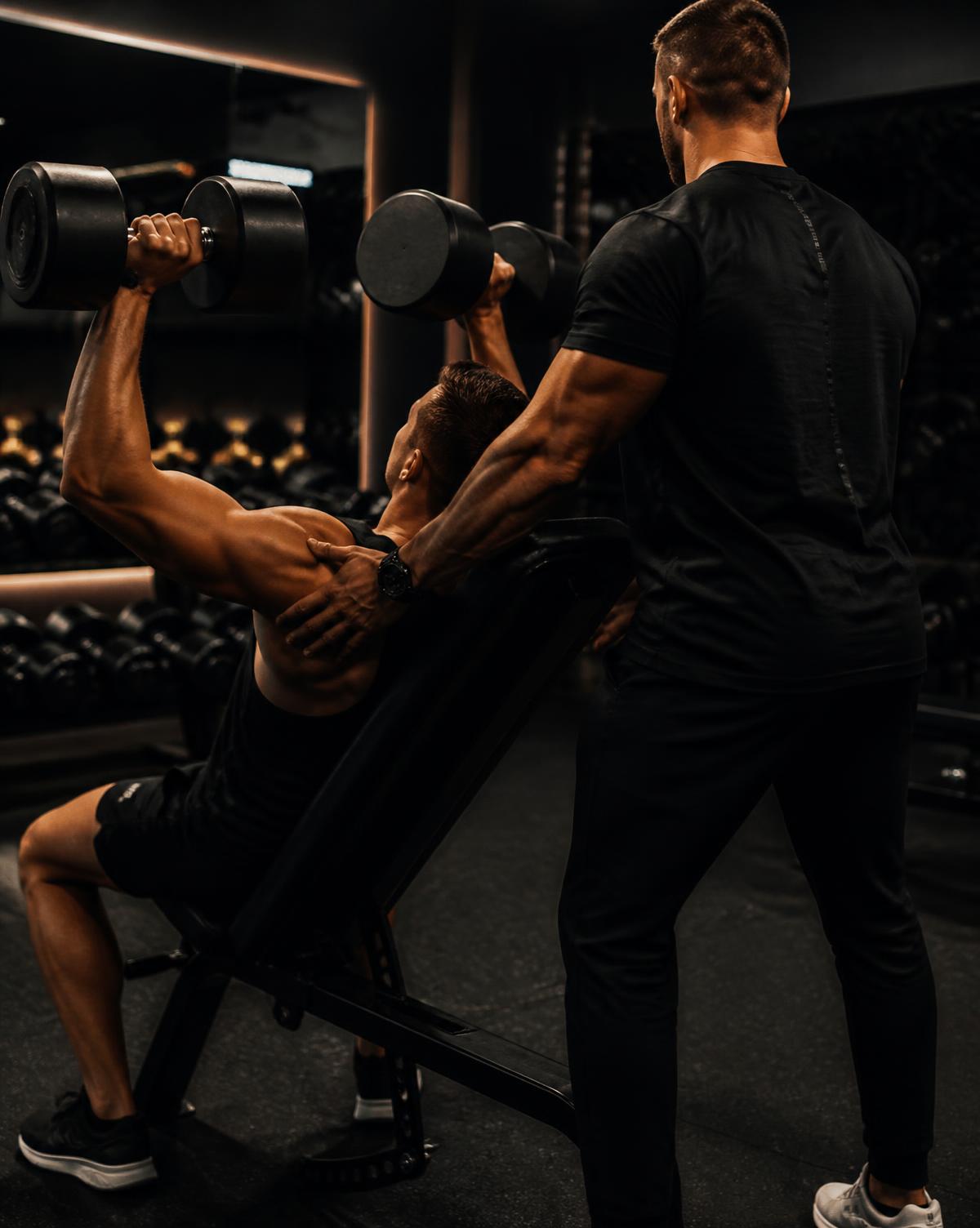 A trainer spotting a client through a dumbbell press in a one-on-one session