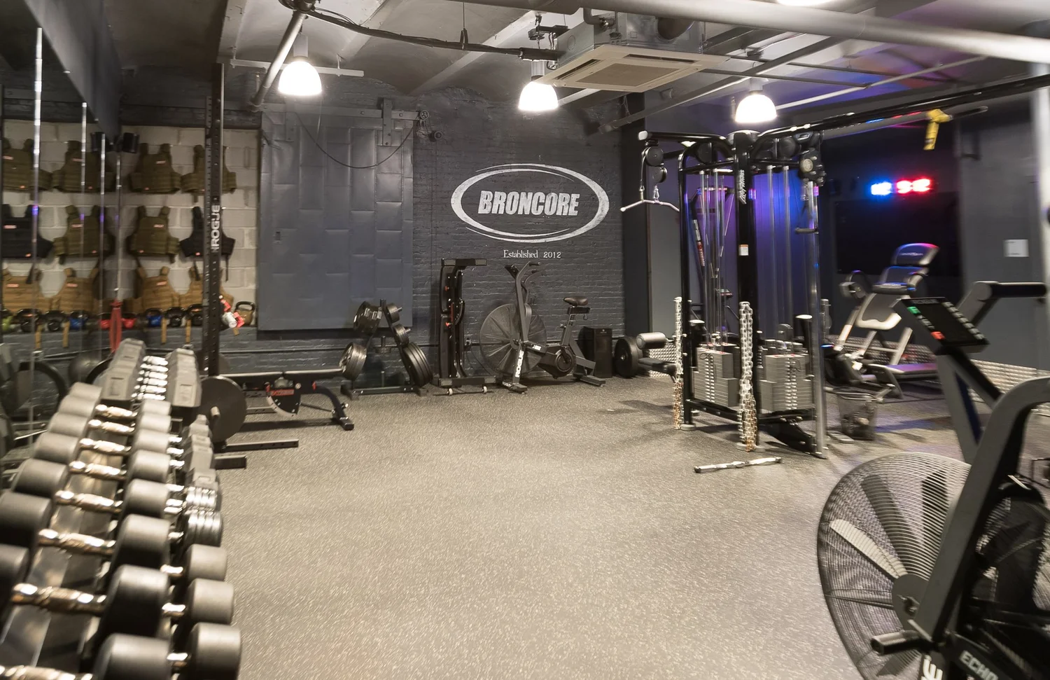 The weight room at BronCore Fitness with dumbbells, benches, racks and bikes
